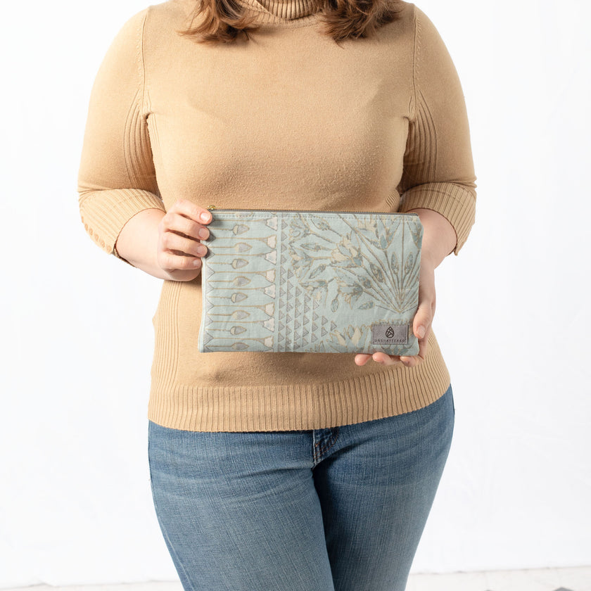 A woman holding a blue print design large zip pouch with a gray label and gold tone zipper