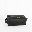 A black toiletry kit with a zipper closure, made from outdoor furniture material  with a textured surface, featuring a small brand tag attached to the zipper.