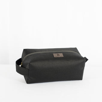 A black toiletry kit with a zipper closure, made from outdoor furniture material  with a textured surface, featuring a small brand tag attached to the zipper.