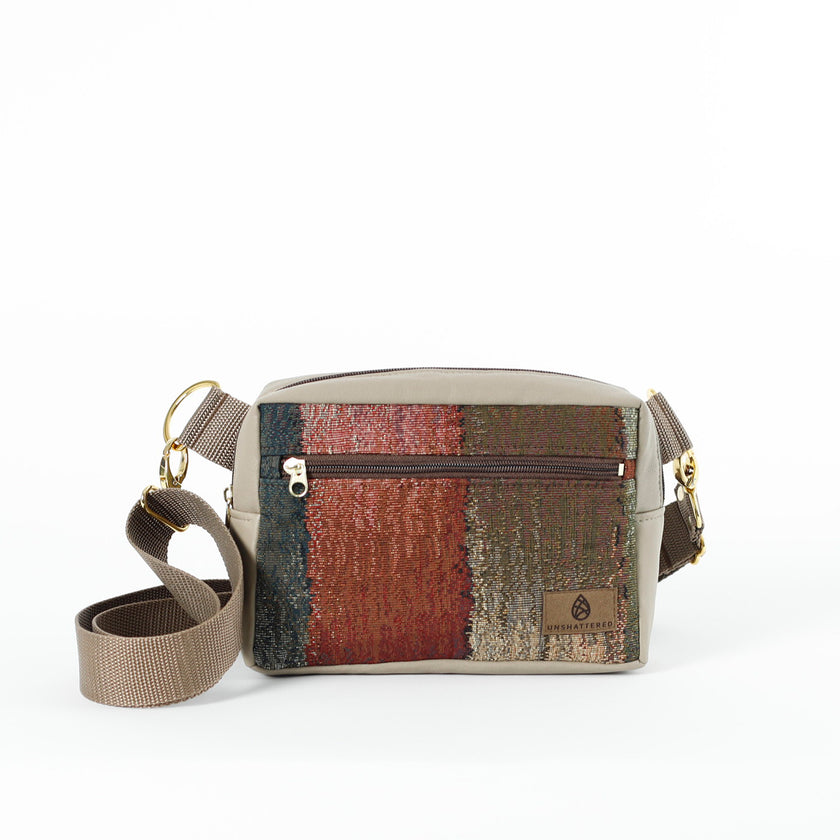 A small crossbody bag with a fall-themed fabric front panel and a gray leather alternative exterior. It includes an adjustable strap, gold-tone hardware, and a front zip pocket.