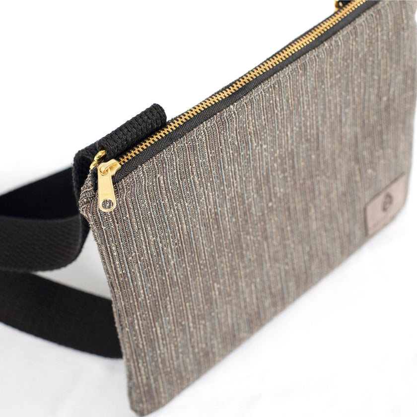 A gold-tone zipper on a textured gray crossbody pouch made from upcycled materials