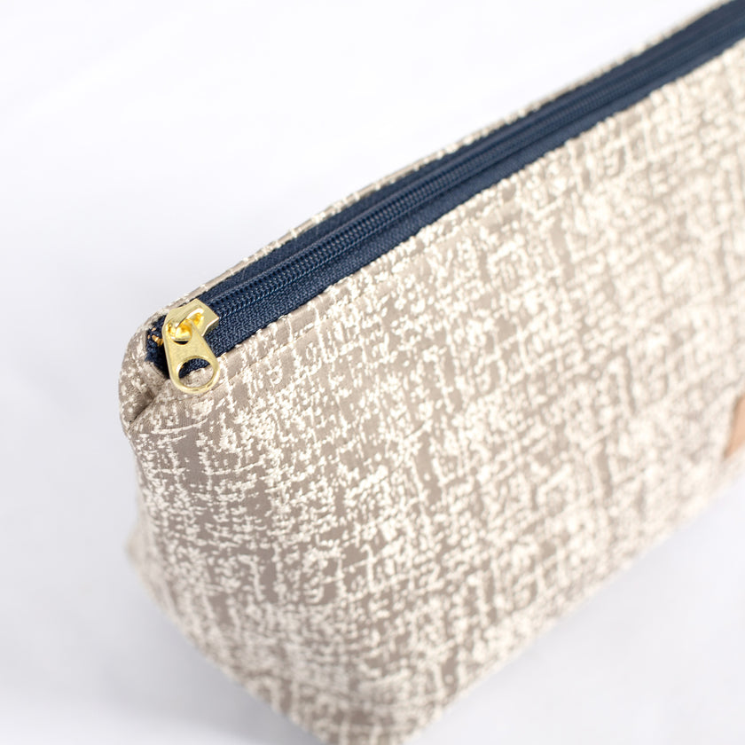 A gold tone zipper on an upcycled neutral fabric makeup bag