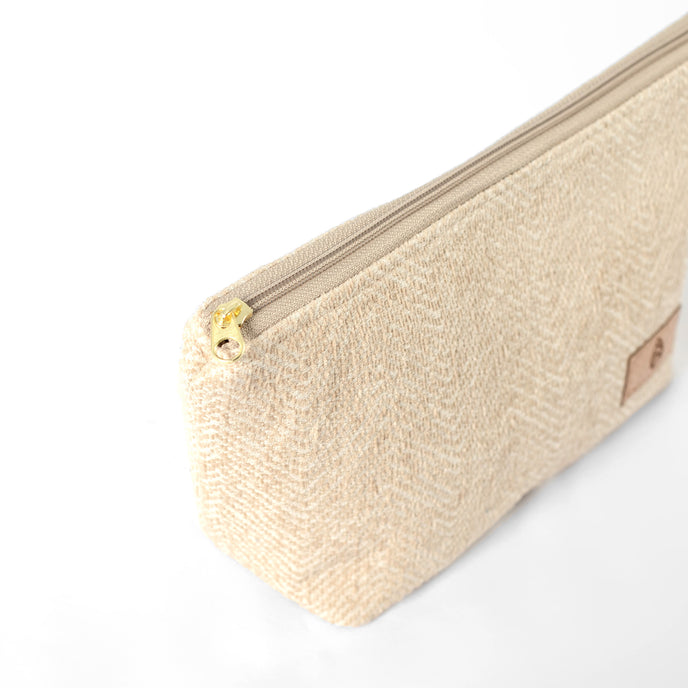 Gold-tone zipper on a makeup bag made from upcycled beige material on a white background
