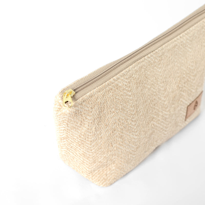 Gold-tone zipper on a makeup bag made from upcycled beige material on a white background