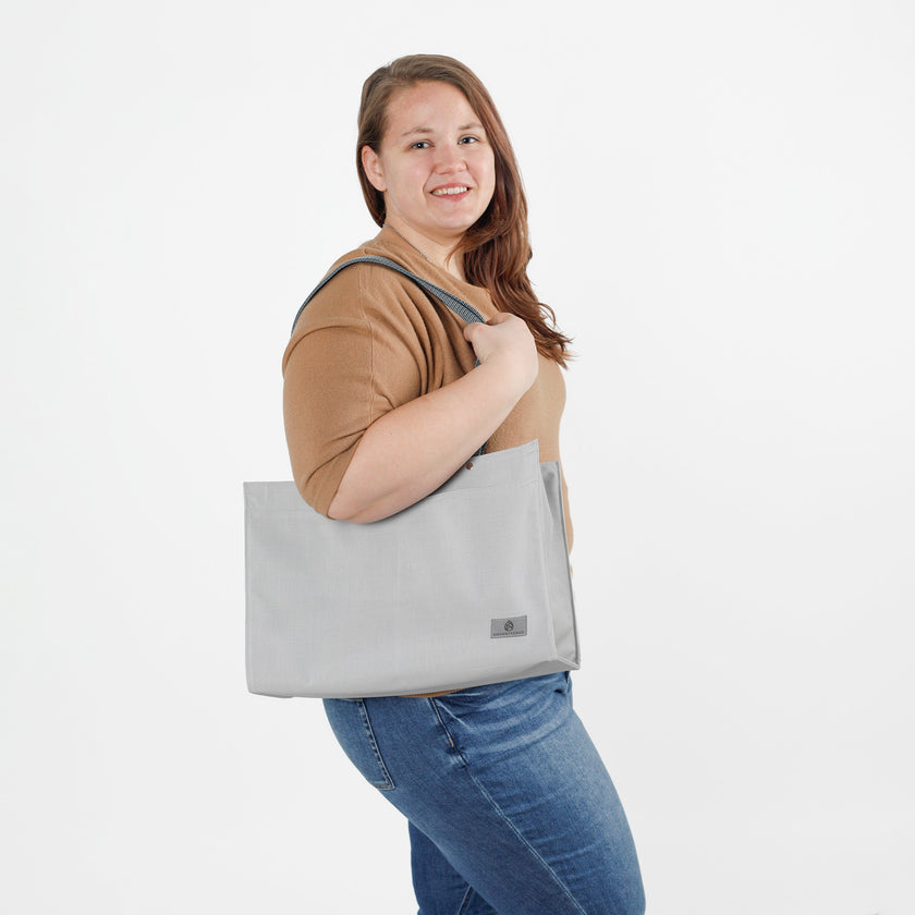Woman holding a gray zippered tote bag against a white background
