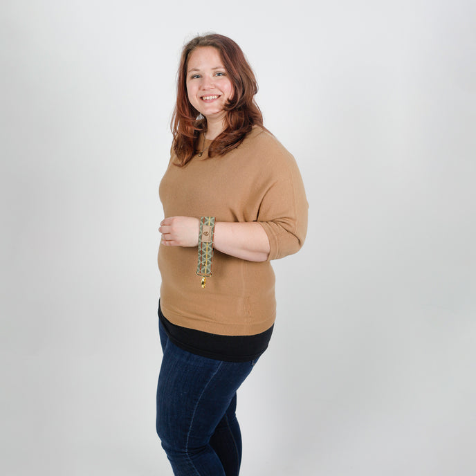 Woman wearing a brown sweater and blue jeans holding key clip on her wrist  a white background