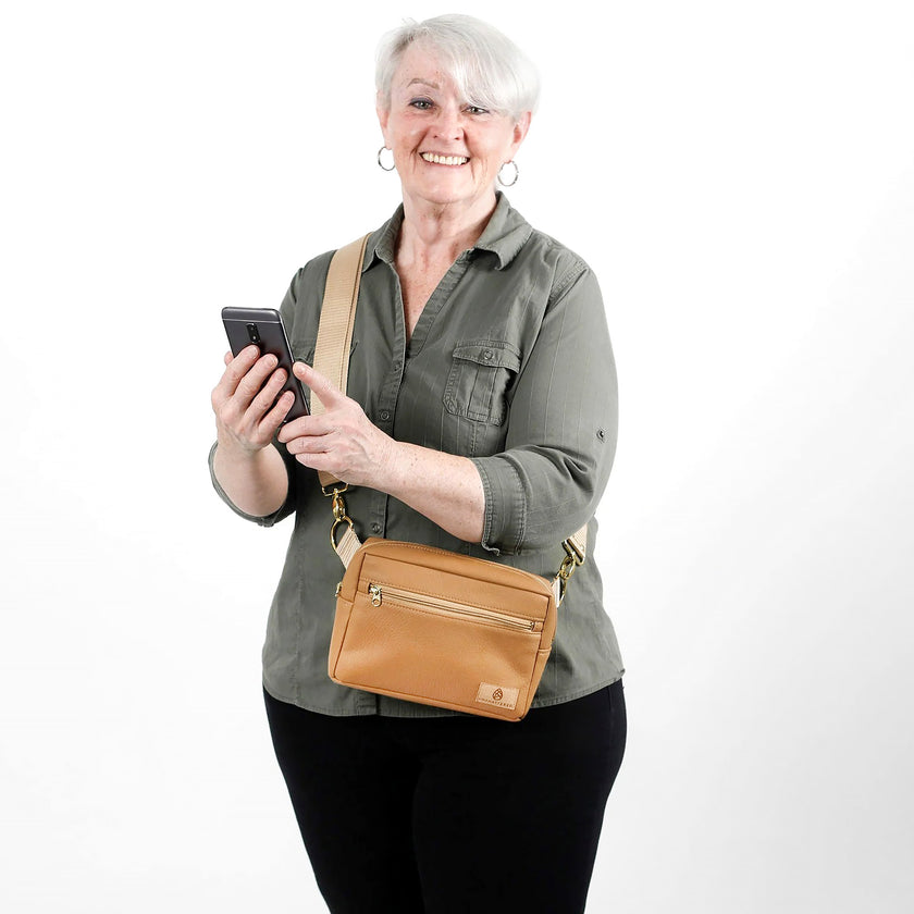 Woman holding a phone with a tan crossbody bag on a white background