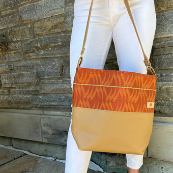 A woman holding this orange fabric tote with a gold seam on the outside