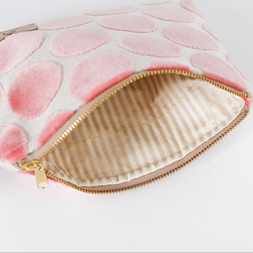 Striped beige interior of a pink polka dot pouch with gold zipper on a white background