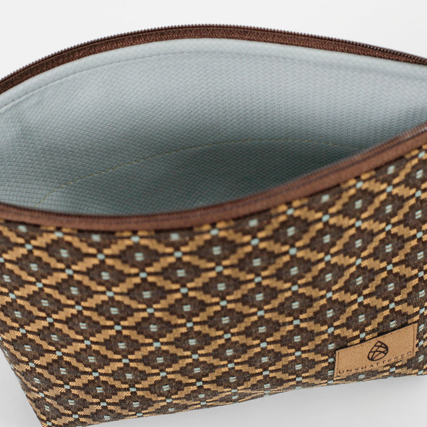 Pale blue, luxury leather alternative interior of a makeup bag with a brown and blue geometric fabric exterior on a white background