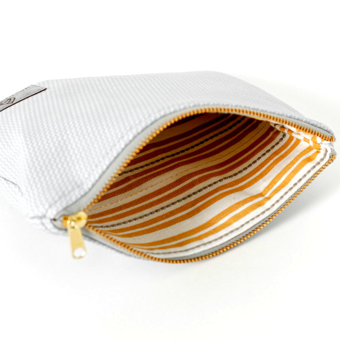 A cream with orange stripes and brown dashes design interior on a silver luxury leather alternative zip pouch, bag named after Irene.