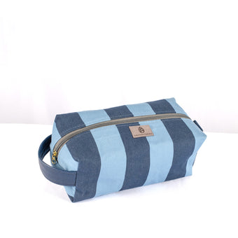 A blue striped toiletry kit with a gold-tone zipper and a handle, made from upcycled fabric named after Jackie 
