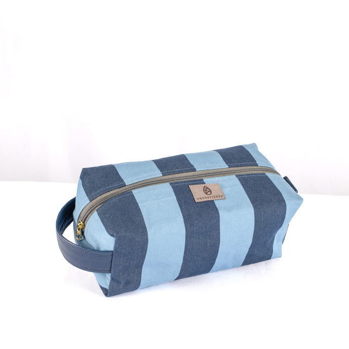 A blue striped toiletry kit with a gold-tone zipper and a handle, made from upcycled fabric named after Jackie 