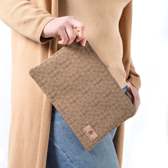 A woman wearing a tan turtleneck and jeans holding a brown geometric design with a tan label