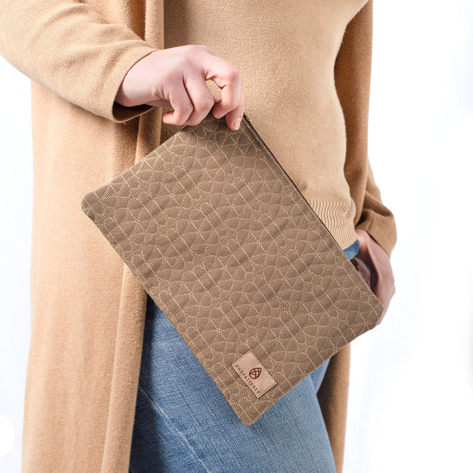 A woman wearing a tan turtleneck and jeans holding a brown geometric design with a tan label