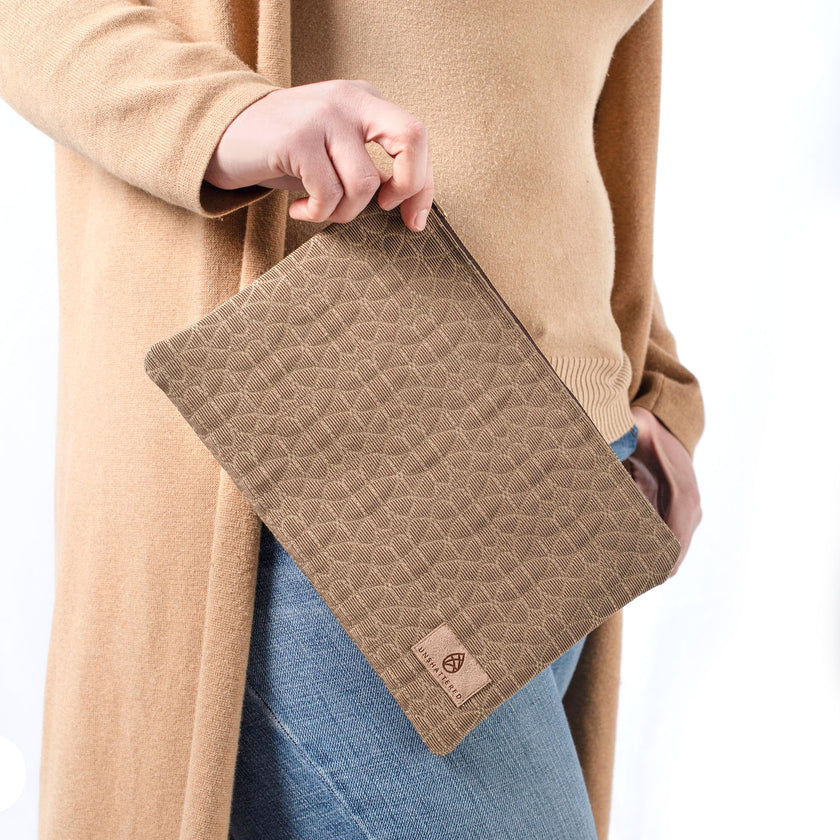 A woman wearing a tan turtleneck and jeans holding a brown geometric design with a tan label