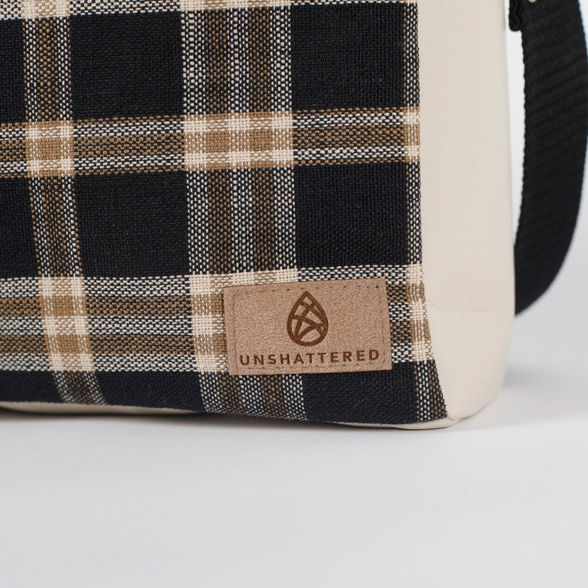 Plaid-patterned bag with 'Unshattered' brand logo on a white background named after Jeanne