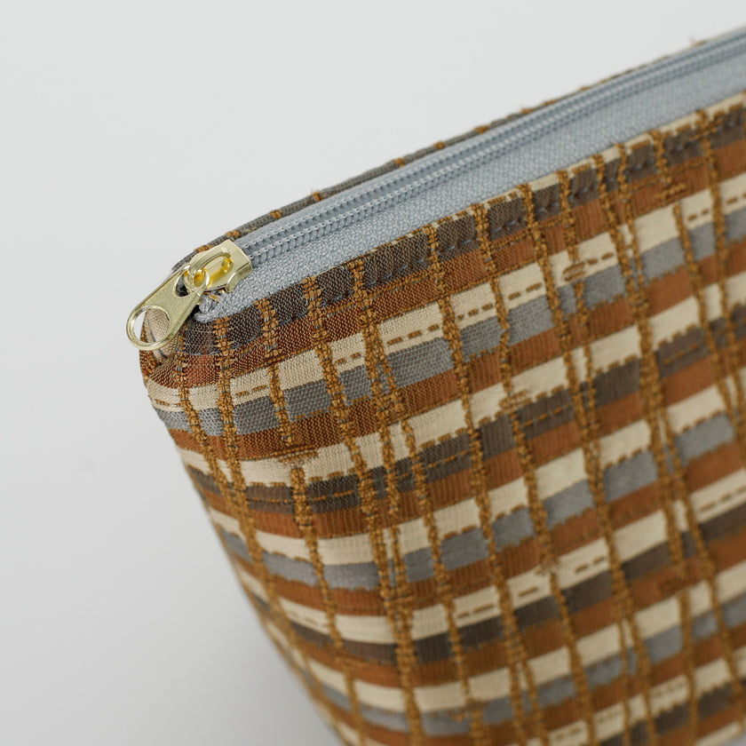 A gold tone zipper on a multi- brown makeup bag