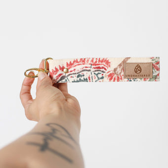 Hand holding a floral-patterned key clip with 'Unshattereds' branding on a white background named after Jeyana 