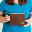 A woman holding a brown suede zip pouch named after Jillian 