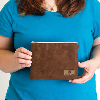A woman holding a brown suede zip pouch named after Jillian 