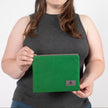 A woman  holding a textured green fabric zip pouch featuring a gray label and a matching gray zipper, shown in a detailed, up-close view to highlight the fabric quality.