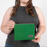A woman  holding a textured green fabric zip pouch featuring a gray label and a matching gray zipper, shown in a detailed, up-close view to highlight the fabric quality.