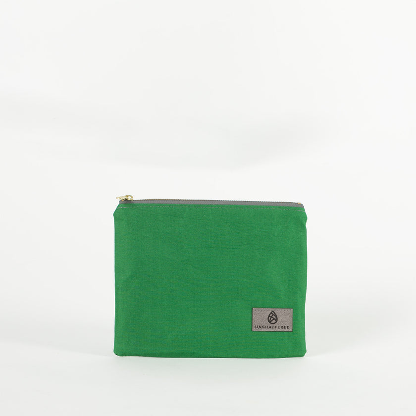 A green zip pouch with a gray Unshattered label on a white background