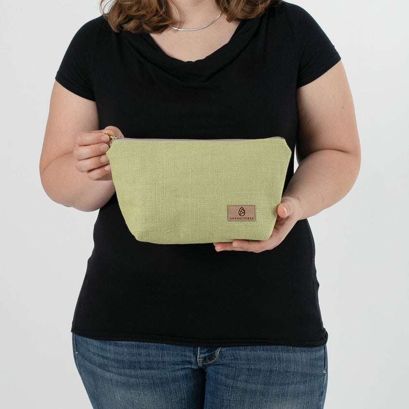 A woman holding a green fabric makeup kit with a tan Unshattered label 