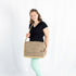 A woman wearing a black shirt with green pants carrying a beige and tan large messenger with circle designs 