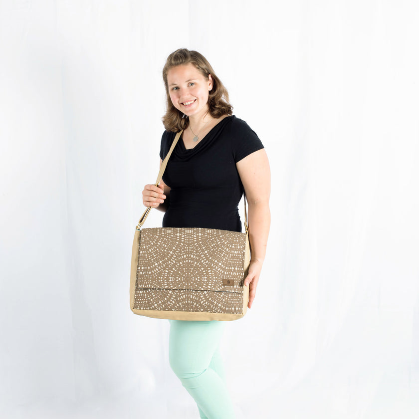 A woman wearing a black shirt with green pants carrying a beige and tan large messenger with circle designs 