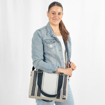A woman carrying a convertible handbag with a beige upcycled fabric, blue stripes, and navy-colored straps with gold-tone hardware.