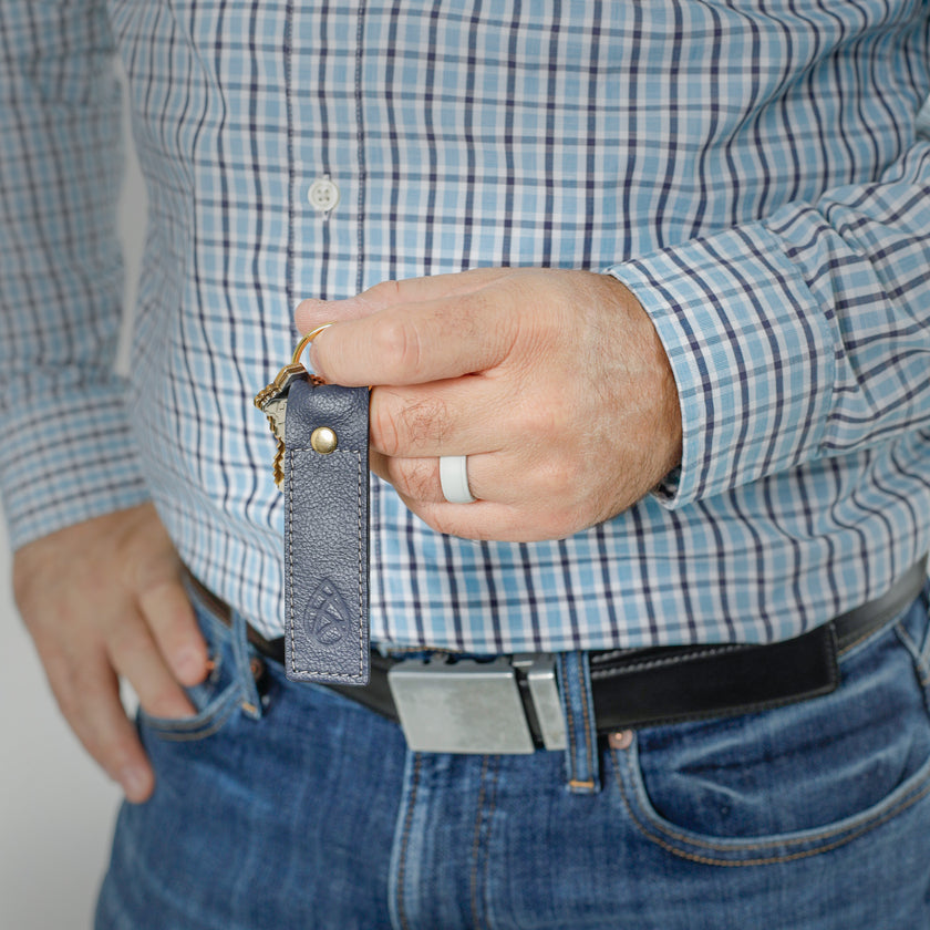 A man holding a Southwest Blue leather keychain with a gold tone hardware 