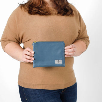 A woman holding a blue luxury leather alternative zip pouch with a gray Unshatered label 