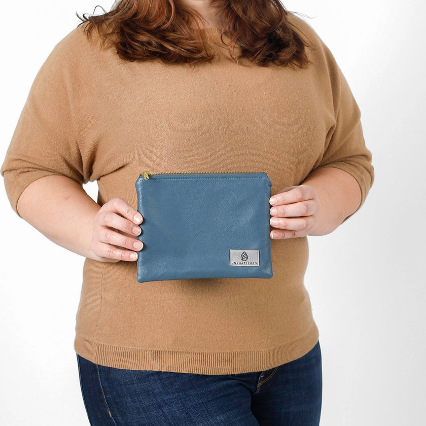 A woman holding a blue luxury leather alternative zip pouch with a gray Unshatered label 