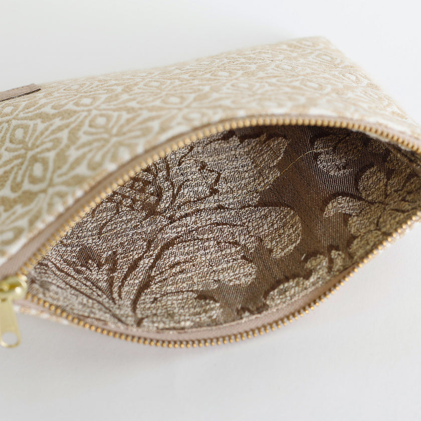Close-up of interior of a beige patterned pouch with a gold zipper on a white background