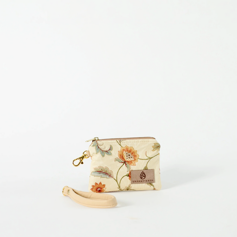 A tan clip pouch with floral designs, a wristlet strap, and gold-tone hardware, displayed against a white background named after Kat 