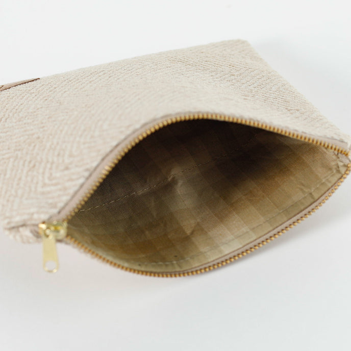 A tan multi-color checkered fabric with a gold seam on a beige zip pouch with gold tone zipper