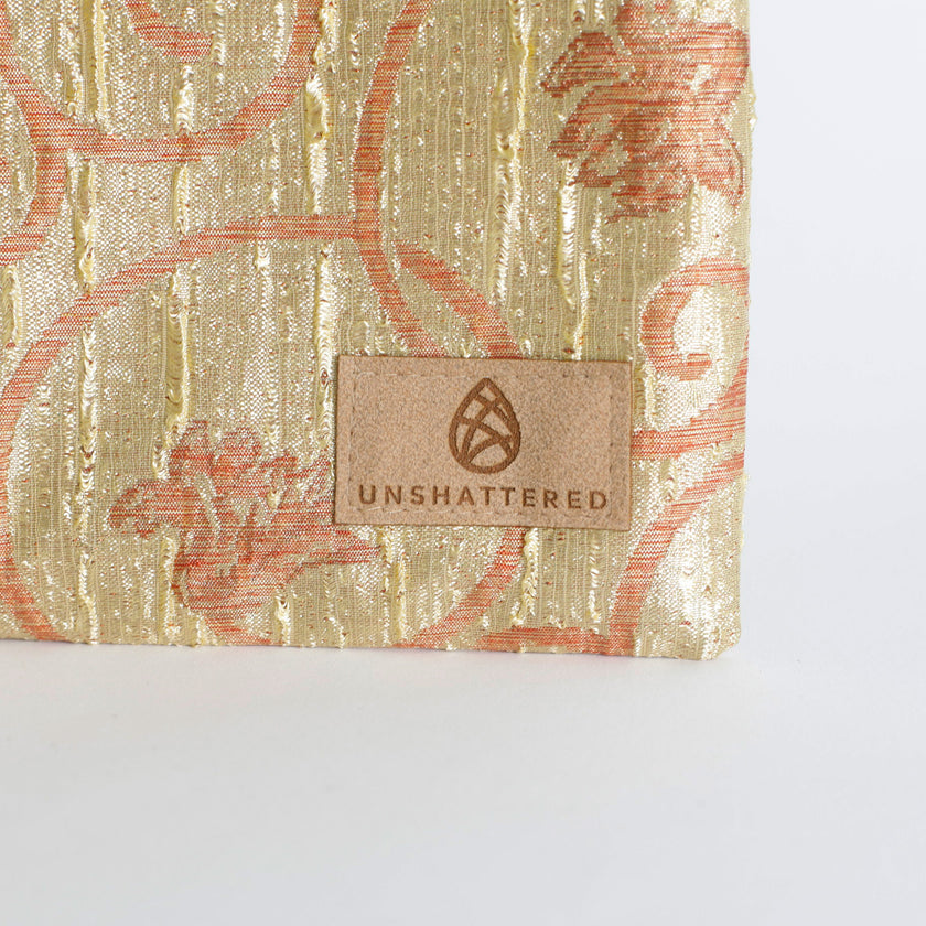 Shimmery gold zip pouch with 'Unshattered' brand label on a white background