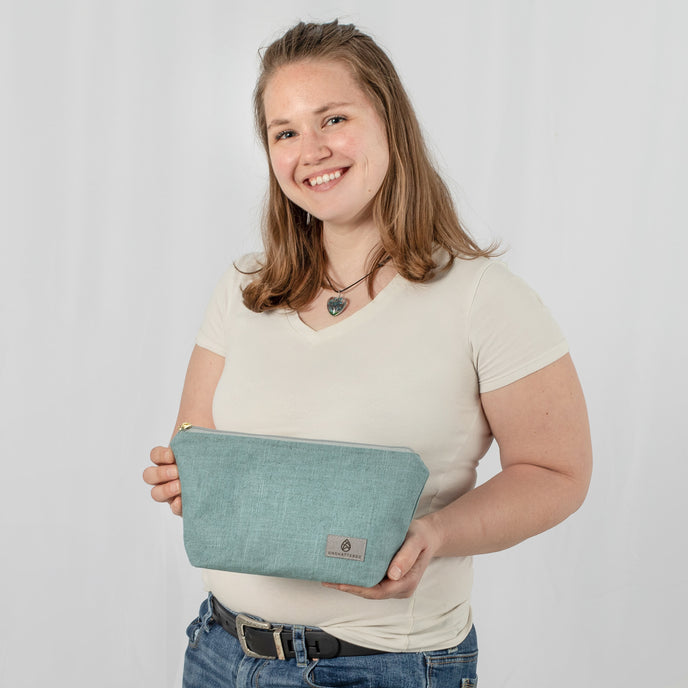 A woman holding a blue makeup bag with a zip closure and a gray Unshattered label named after Kelly.