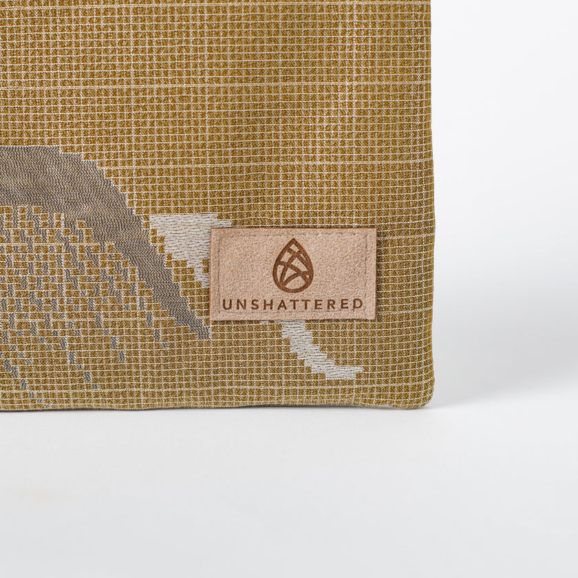 Textured beige zip pouch with 'Unshattered' logo on a white background