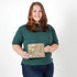 Woman holding a small, beige zip pouch against a plain background