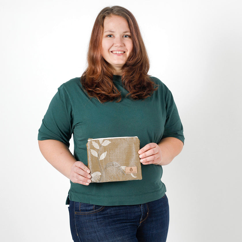 Woman holding a small, beige zip pouch against a plain background