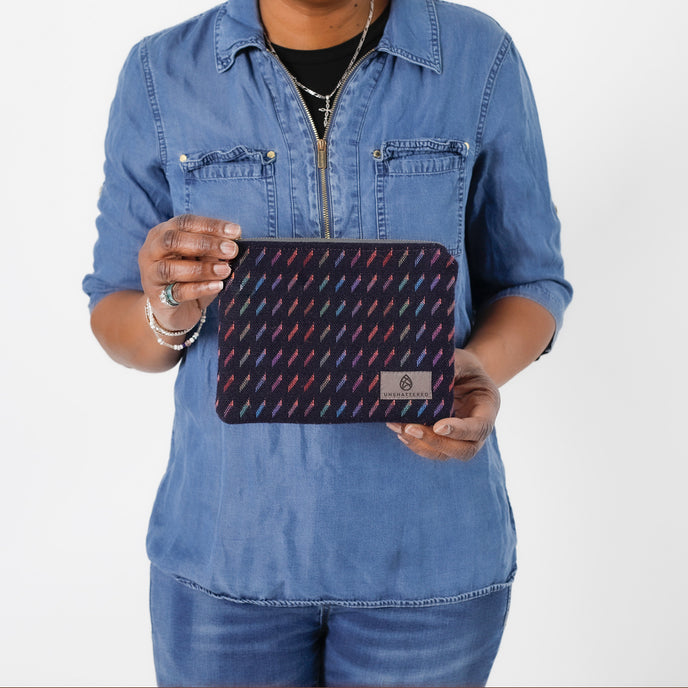 A woman holding a dark blue zip pouch with lines in multi-colors named after Keri 