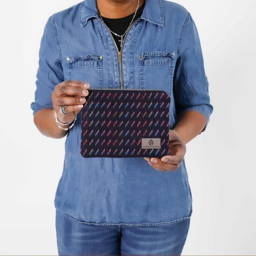 A woman holding a dark blue zip pouch with lines in multi-colors named after Keri 