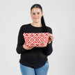A woman holding a red and white design makeup bag wearing a black long sleeve shirt with jeans named after Keyrah