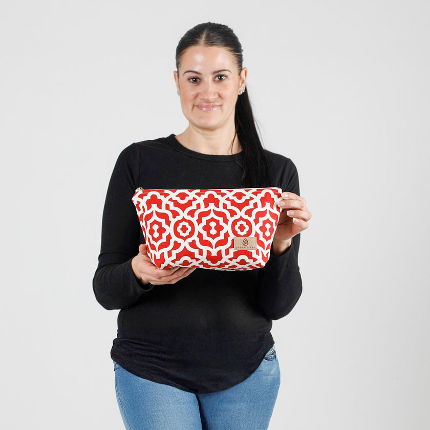 A woman holding a red and white design makeup bag wearing a black long sleeve shirt with jeans named after Keyrah