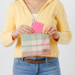 A woman holding a pink picnic plaid zip pouch putting items into the bag wearing a yellow sweater named after Kim 