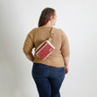 Person wearing a beige sweater and blue jeans with a red errand bag on a white background named after Korin 
