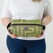 A woman holding a lime green geometric pattern toiletry kit with a gray Unshattered label named after Kristie